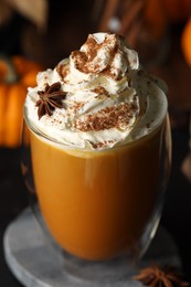 Photo of Glass of pumpkin spice latte with whipped cream and ingredients on black table, closeup