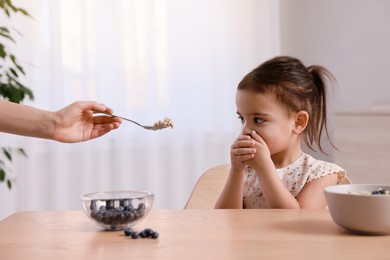 Photo of Cute little girl covering her mouth and refusing to eat breakfast at home