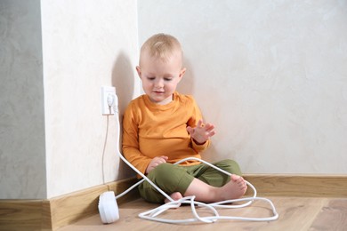 Photo of Little child playing with power strip near electrical socket at home. Dangerous situation