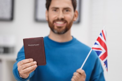 Photo of Immigration. Happy man with passport and flag of United Kingdom indoors, selective focus