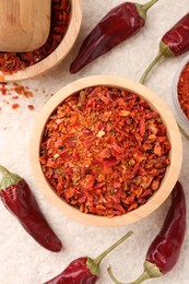 Photo of Chili pepper flakes and pods on light textured table, flat lay