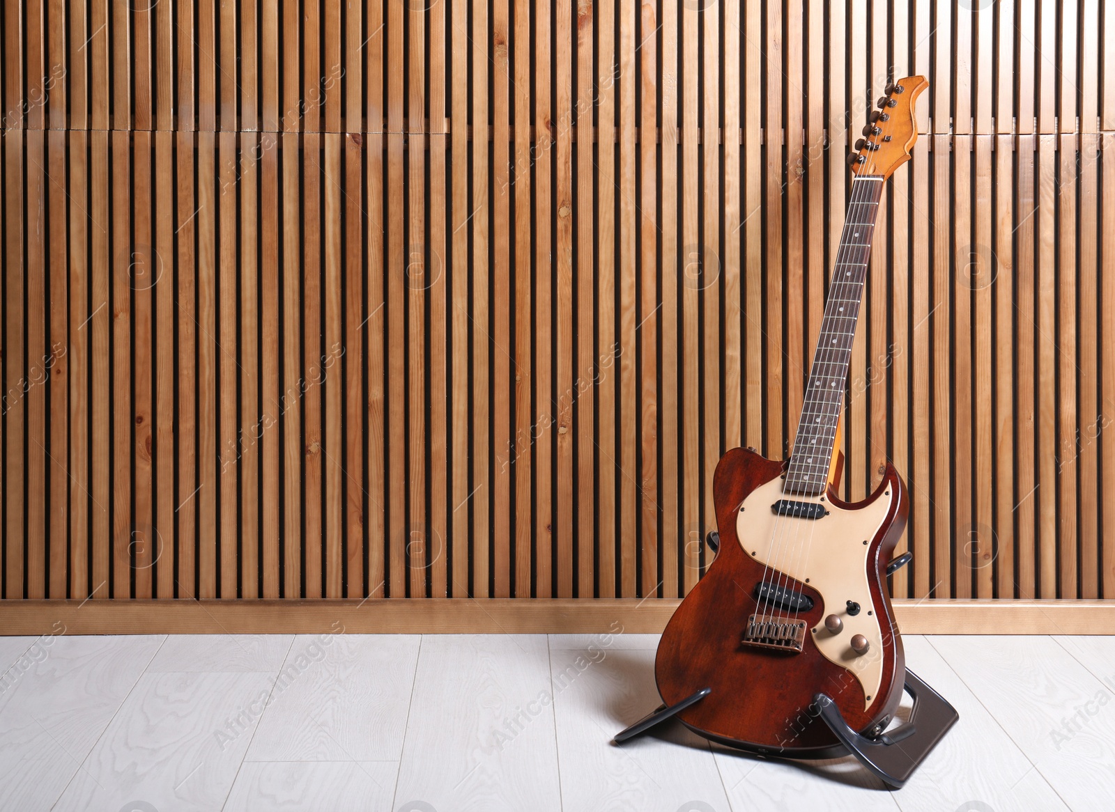 Photo of Stand with electric guitar near wooden wall. Space for text