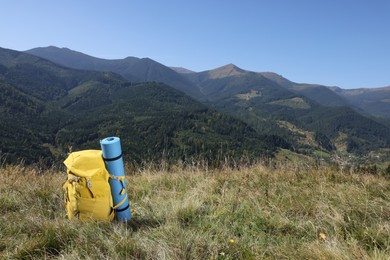 Backpack and sleeping pad in mountains on sunny day, space for text