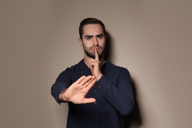 Man showing HUSH gesture in sign language on color background