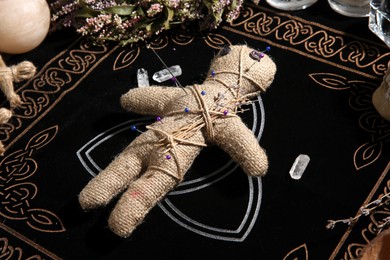 Photo of Voodoo doll pierced with pins surrounded by ceremonial items on table. Curse ceremony