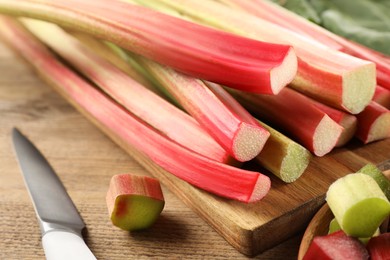 Photo of Many cut rhubarb stalks and knife on wooden table, closeup