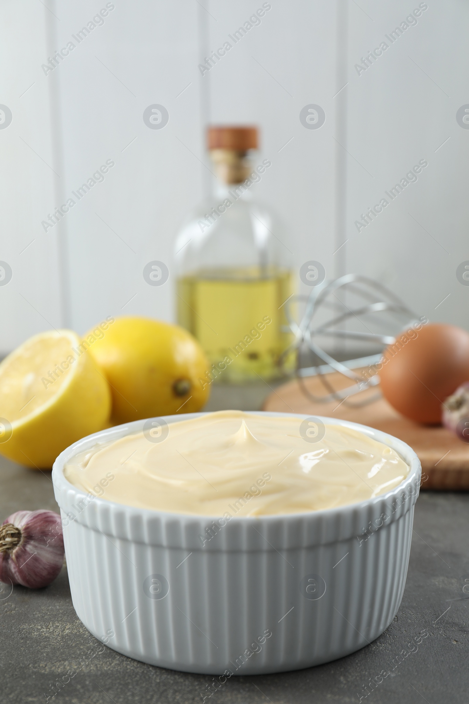 Photo of Fresh mayonnaise sauce in bowl and ingredients on grey table