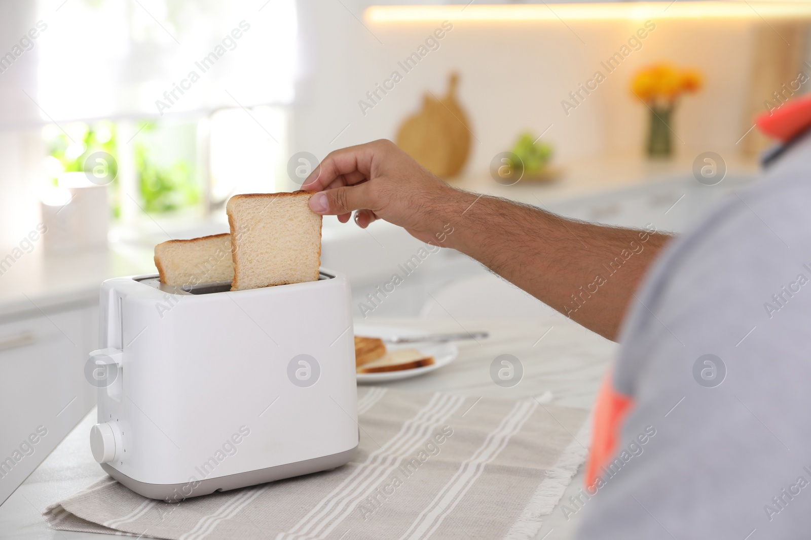 Photo of Man using toaster at table in kitchen, closeup