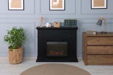 Photo of Black stylish fireplace between potted plant and chest of drawers in cosy living room