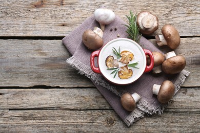 Photo of Delicious homemade mushroom soup in ceramic pot and fresh ingredients on wooden table, flat lay. Space for text