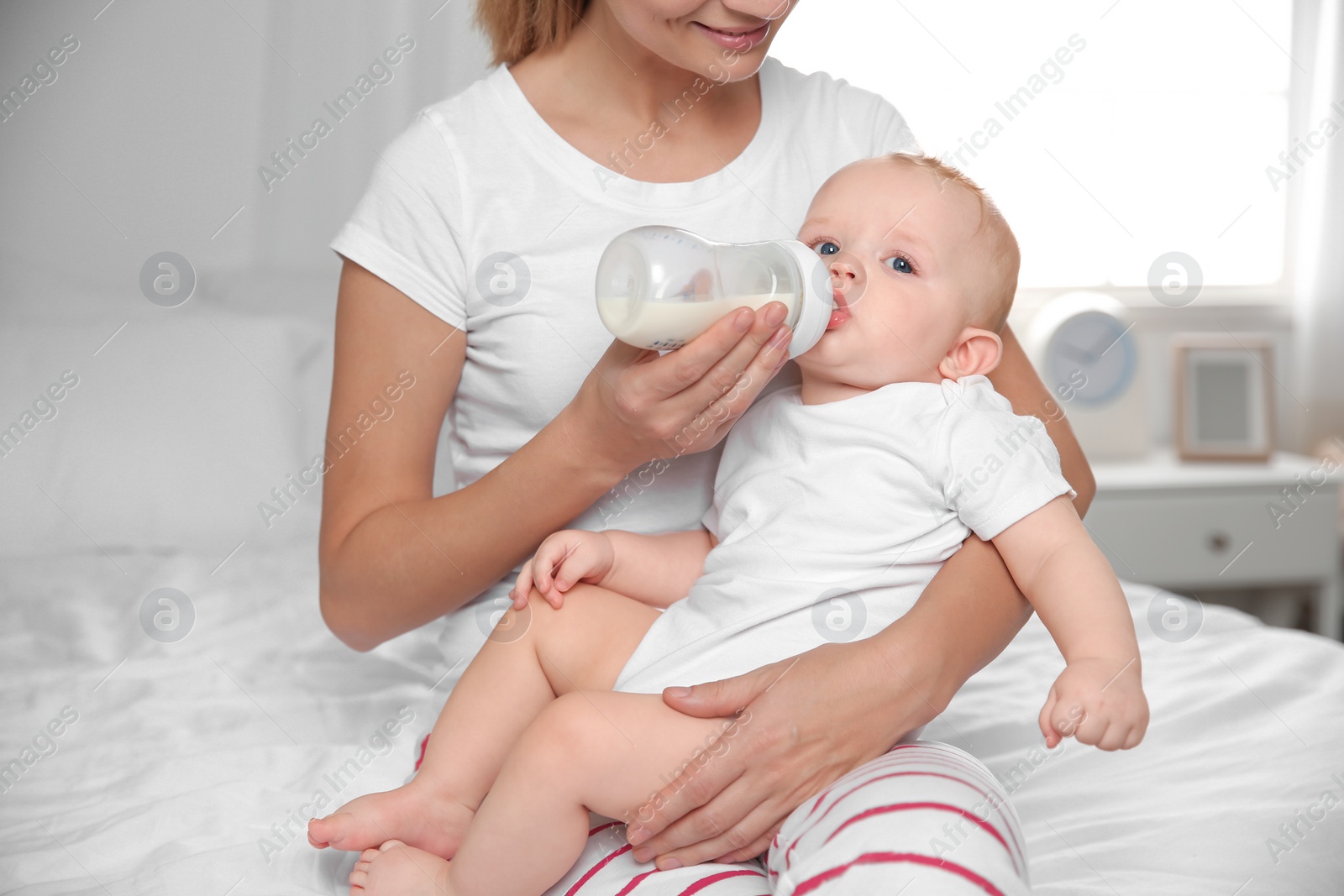 Photo of Lovely mother holding and feeding her baby from bottle on bed at home