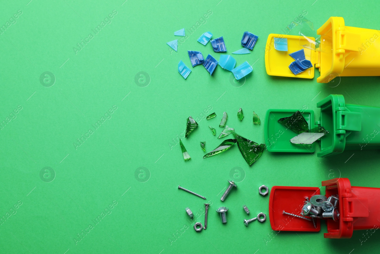 Photo of Mini recycling bins and different garbage on green background, flat lay with space for text. Waste sorting