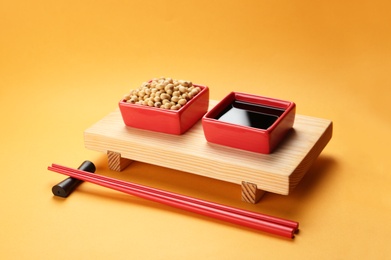 Photo of Bowls of soy sauce and beans on stand with chopsticks against color background