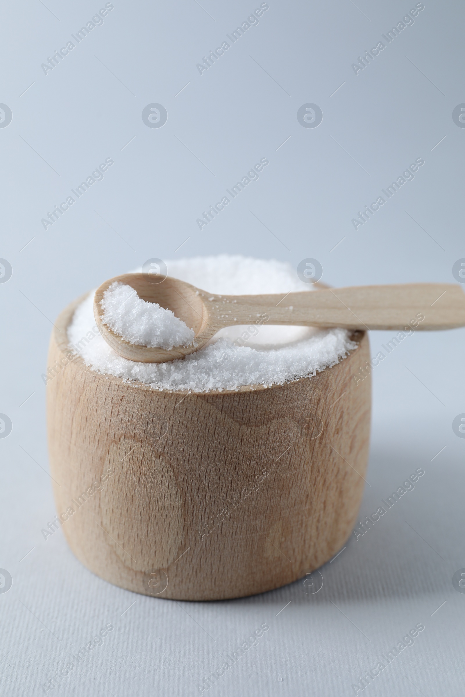 Photo of Organic white salt in bowl and spoon on light grey background, closeup. Space for text