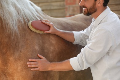 Man brushing adorable horse outdoors, closeup. Pet care