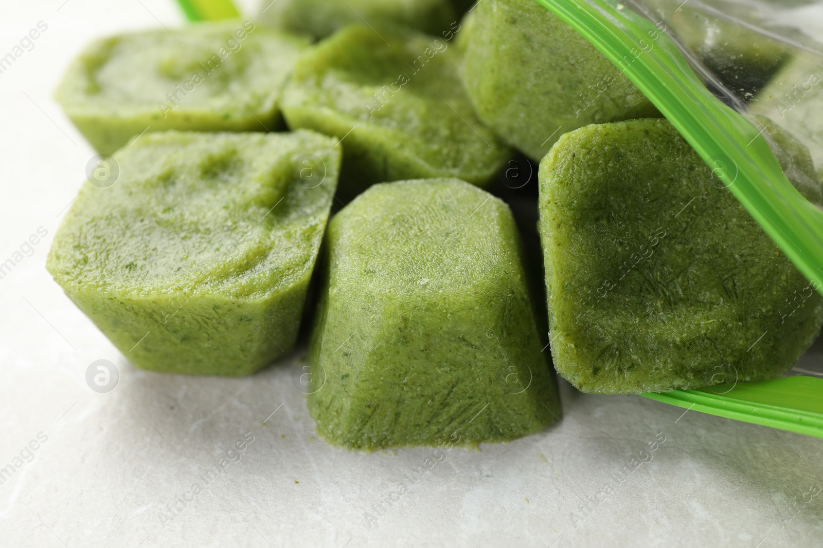 Photo of Frozen broccoli puree cubes in plastic bag on table, closeup