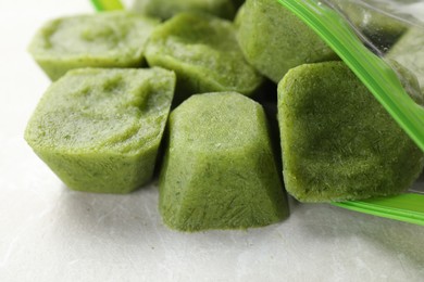 Photo of Frozen broccoli puree cubes in plastic bag on table, closeup