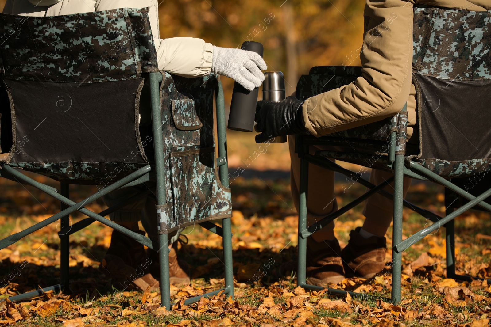 Photo of Couple with thermoses sitting in camping chairs outdoors on autumn sunny day, closeup