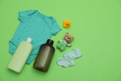 Bottles of laundry detergents, baby clothes and toys on light green background, flat lay. Space for text