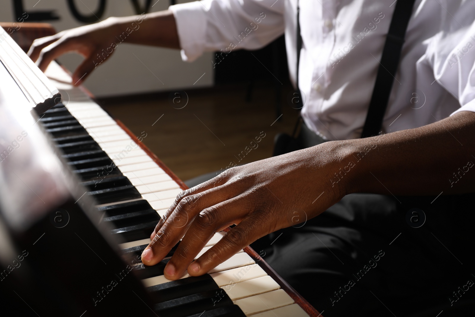 Photo of African-American man playing piano indoors, closeup. Talented musician