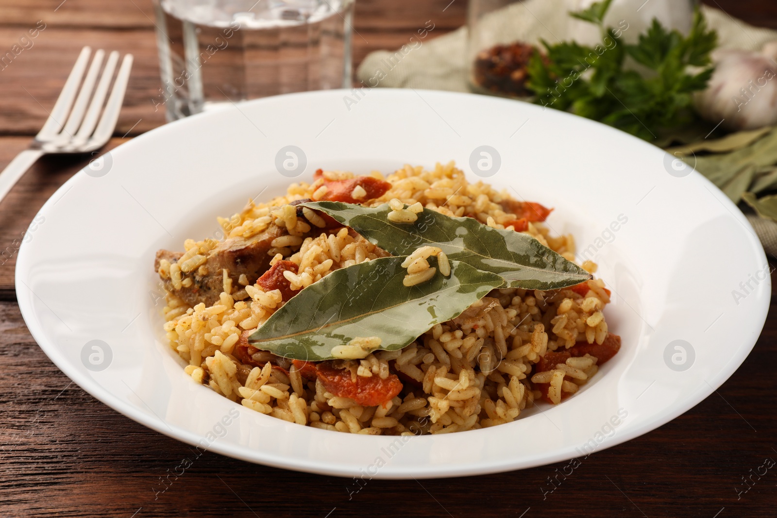Photo of Delicious pilaf and bay leaves on wooden table, closeup
