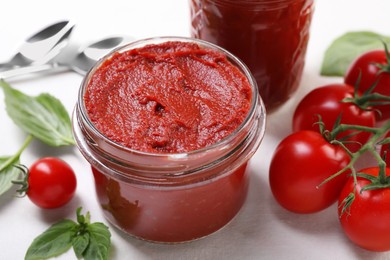 Jar of tasty tomato paste and ingredients on white table, closeup
