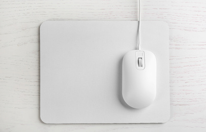 Modern wired optical mouse and pad on white wooden table, top view