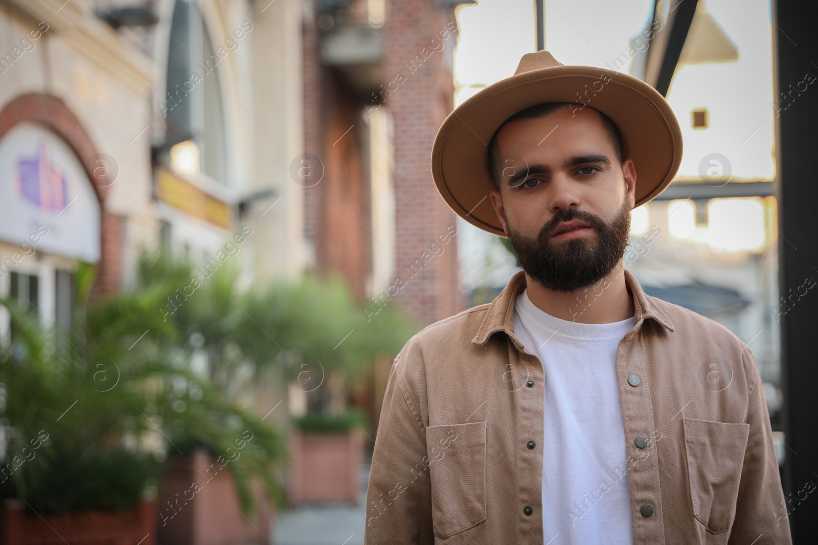 Photo of Portrait of handsome bearded man in hat on city street. Space for text