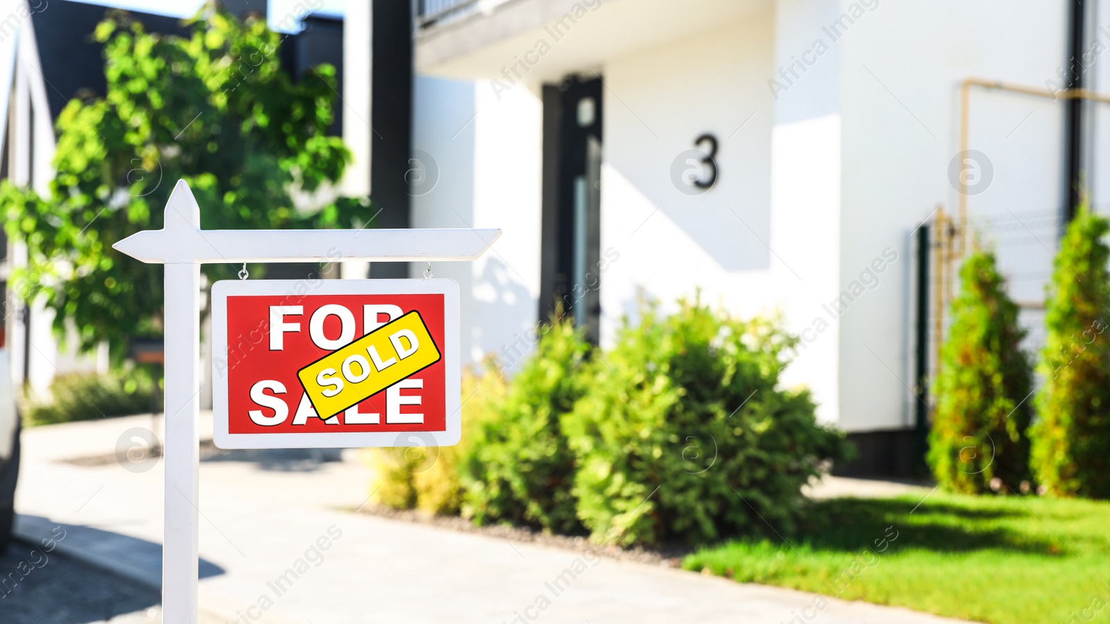 Photo of Red real estate sign near house outdoors on sunny day