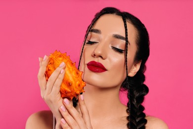 Young woman with fresh kiwano on pink background. Exotic fruit