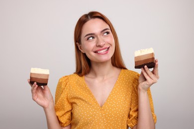 Young woman with pieces of tasty cake on light grey background