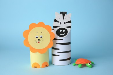 Photo of Toy lion, zebra made from toilet paper hubs and plasticine turtle on light blue background. Children's handmade ideas