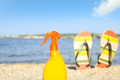 Photo of Bottle of sun protection body cream and slippers on beach, space for design