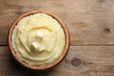 Bowl of delicious mashed potato with butter on wooden table, top view. Space for text