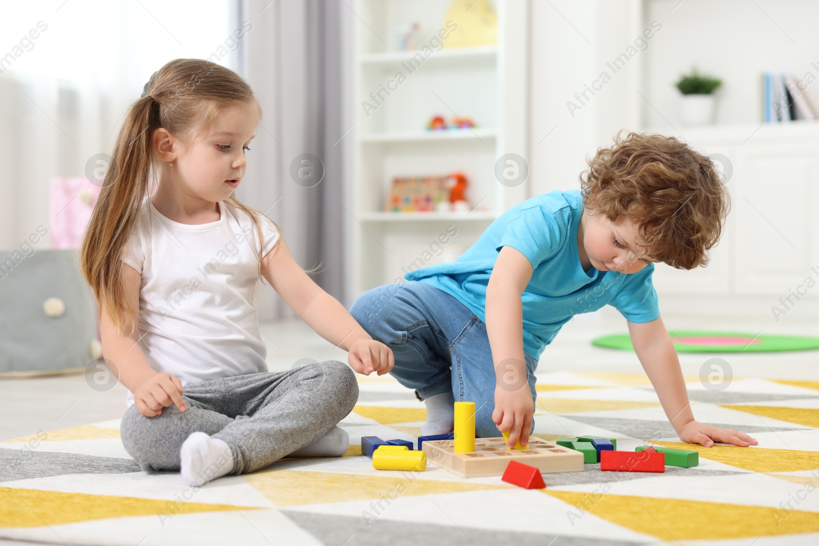 Photo of Cute little children playing with set of wooden geometric figures on floor in kindergarten
