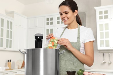 Photo of Woman putting vacuum packed vegetables into pot with sous vide cooker in kitchen. Thermal immersion circulator