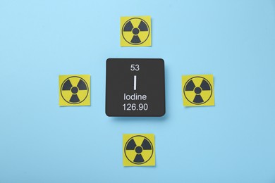 Photo of Card with chemical element Iodine and radiation signs on light blue background, flat lay