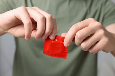 Closeup view of man opening pack with condom on blurred background