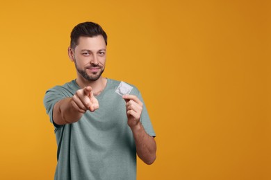 Handsome man holding condom on orange background. Space for text