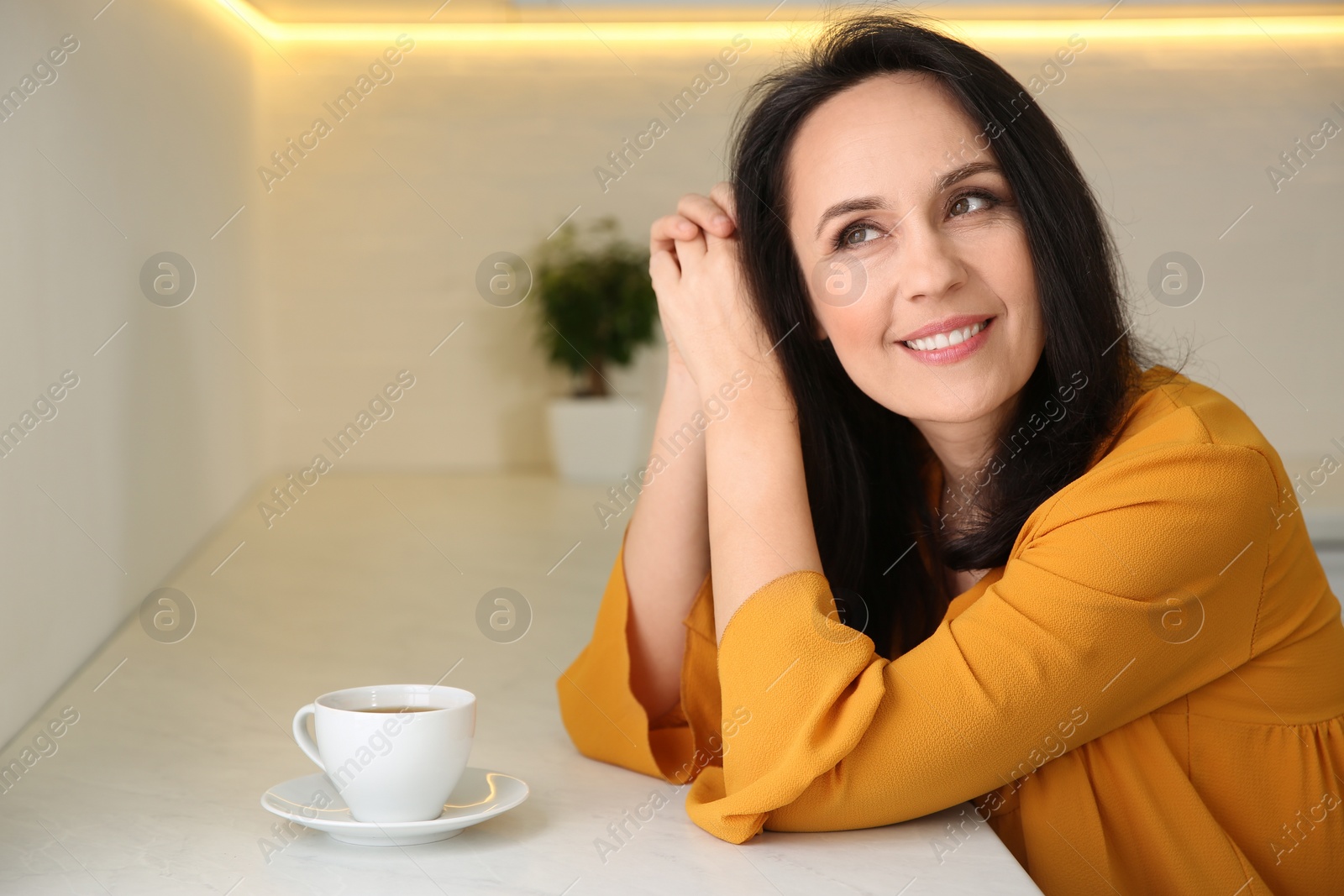 Photo of Beautiful mature woman with cup of coffee at home. Space for text