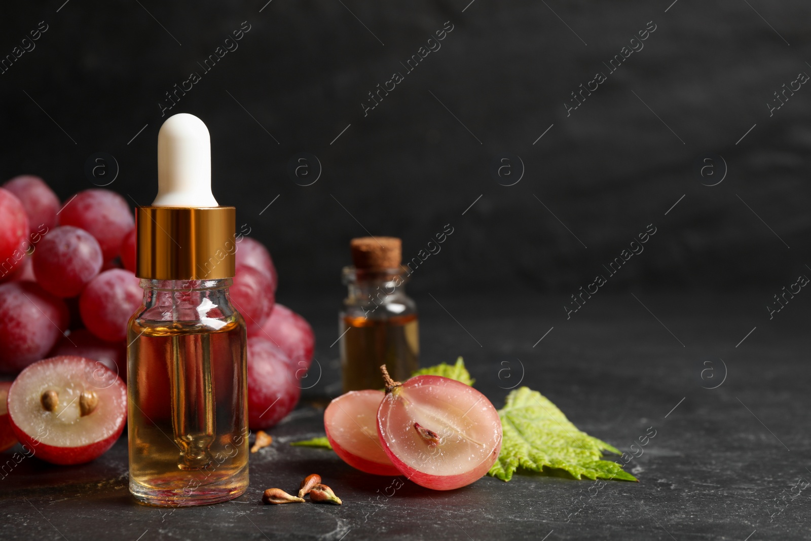 Photo of Bottle of natural grape seed oil on dark table, space for text. Organic cosmetic