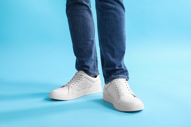 Photo of Man wearing stylish white sneakers on light blue background, closeup