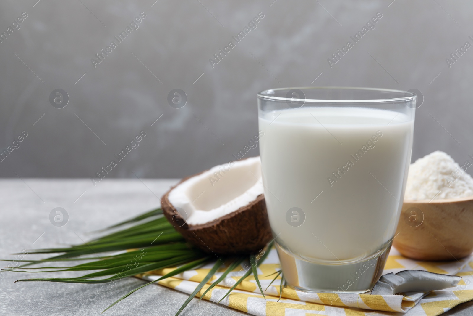 Photo of Glass of delicious coconut milk, flakes, palm leaf and coconut on light grey table, space for text