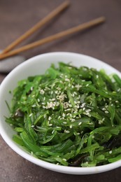 Photo of Tasty seaweed salad in bowl served on brown table, closeup