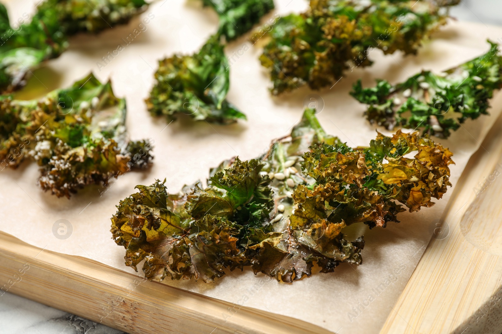 Photo of Tasty baked kale chips on wooden board, closeup