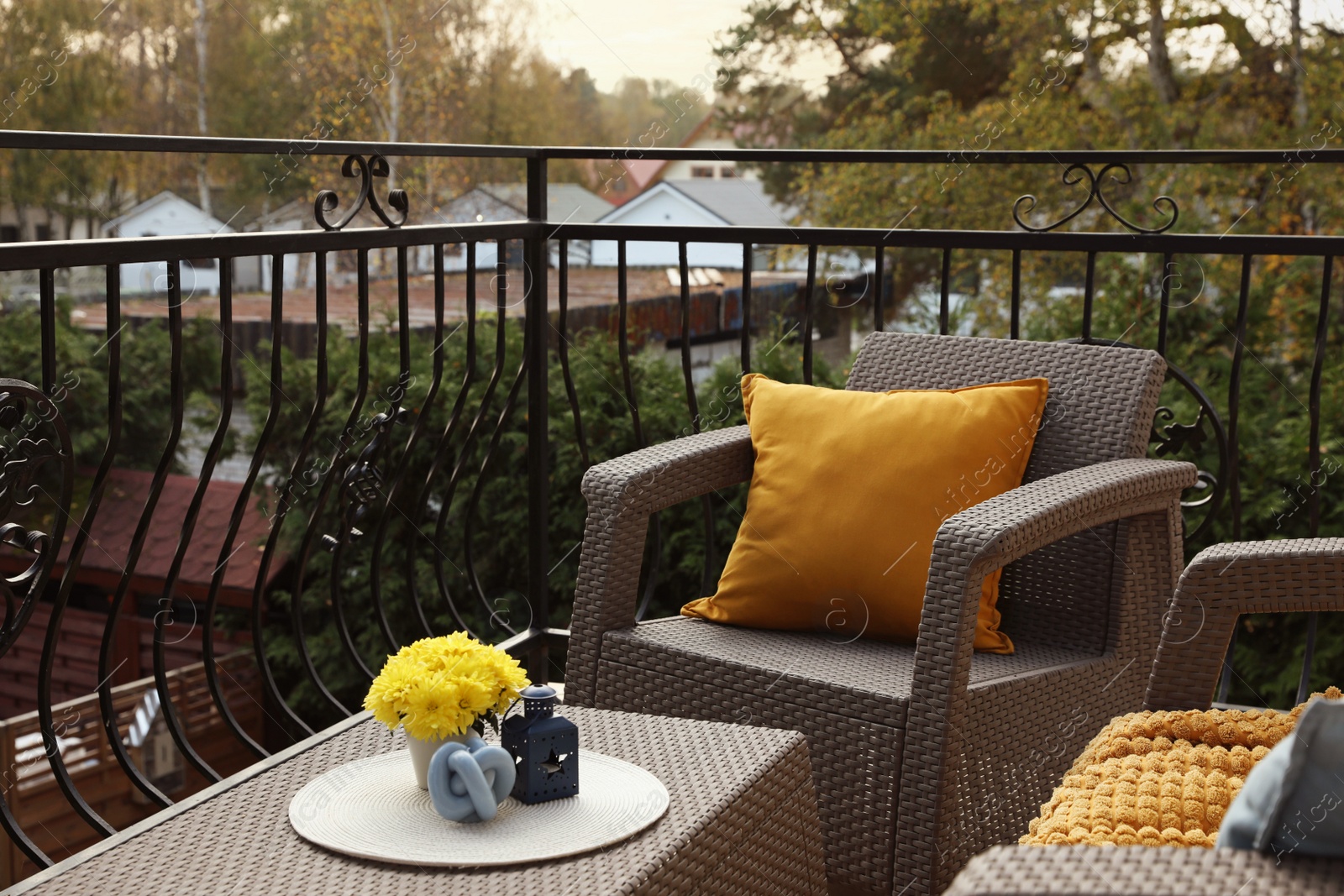 Photo of Orange pillow and yellow chrysanthemum flowers on rattan garden furniture outdoors