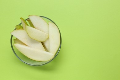 Sliced fresh pear in bowl and space for text on green background, top view. Finger food