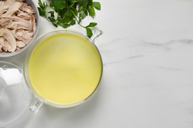 Glass pot with tasty bouillon, chicken and parsley on white marble table, flat lay. Space for text