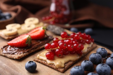 Photo of Fresh crunchy rye crispbreads with different toppings on wooden board, closeup