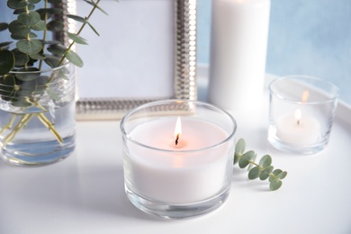 Photo of Burning aromatic candle and eucalyptus branch on table